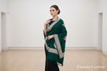 A green Kashmiri embroidered pashmina scarf with tassels on the ends, displayed on a wooden surface.