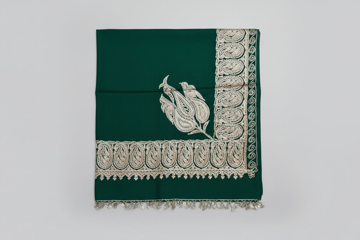 A green Kashmiri embroidered pashmina shawl with tassels on the ends, displayed on a wooden surface.