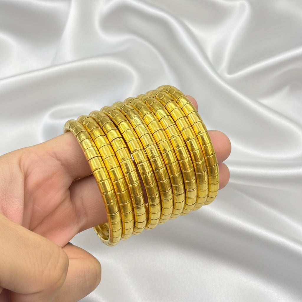 A hand holding a stack of multiple gold-plated segmented bangles against a black background.