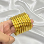 A hand holding a stack of multiple gold-plated segmented bangles against a black background.