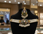 A handcrafted brass choker set displayed on a jewelry stand against a neutral background. The shot clearly shows the arrangement of multi-color sugar stones, white Kundan stones, and the pearl fringe at the base of the necklace and earrings.