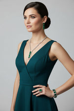 A jewellery set showcasing an asymmetric design, with green stones and silver-colored metal on a mannequin bust.