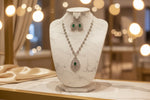 A mannequin showcasing a necklace and earrings set with leaf designs, featuring American diamonds and emerald green semi-precious stones.
