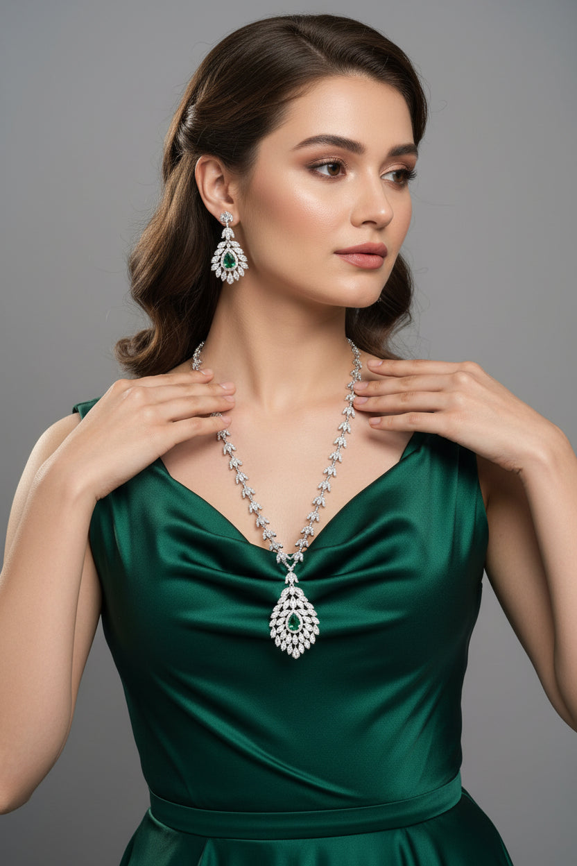 A mannequin showcasing a necklace and earrings set with leaf designs, featuring American diamonds and emerald green semi-precious stones. Party wear set.