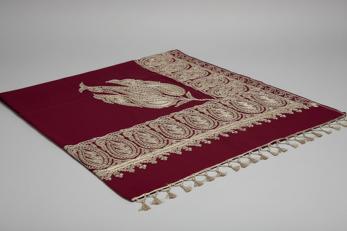 A maroon colour Kashmiri embroidered pashmina shawl with tassels on the ends, displayed on a wooden surface.