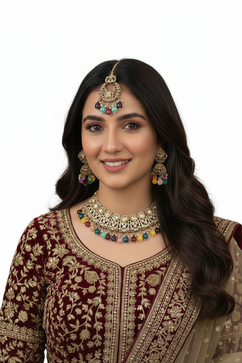 A model in a maroon embroidered velvet outfit wearing a luxury kundan jewelry set with vibrant, multi-colored gemstone drops against a dark velvet backdrop.