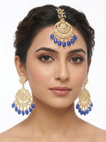 A model wearing a coordinating royal blue and gold Maang Tikka and matching large Chaand Bali earrings.