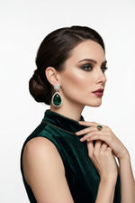 A model wearing elegant pear-cut emerald drop earrings with a diamond halo, styled with a matching green velvet dress.