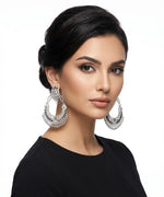 A model wearing large, ornate silver-toned filigree statement earrings with a black top.