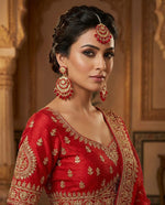A model wearing large rose gold plated earrings with kundan stonework and vibrant red bead droplets.