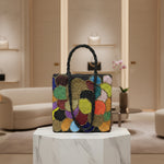 A multi-coloured circular handcrafted tote bag with glass beads, displayed on a wooden surface with foliage in the background.