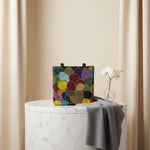 A multi-coloured circular handcrafted tote bag with glass beads, displayed on a wooden surface with foliage in the background
