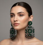 A pair of black earrings with bottle green stones coloured stone embellishments, displayed on an earring stand.