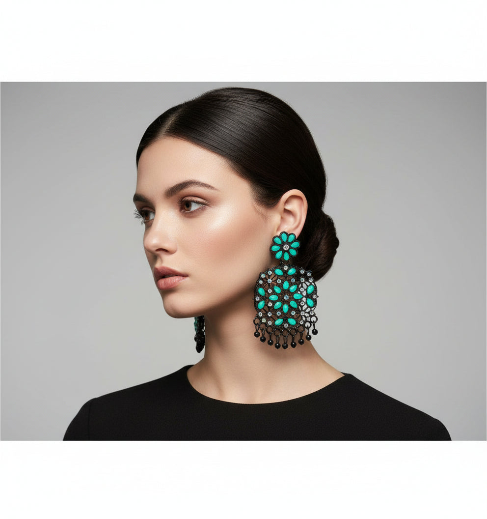 A pair of black earrings with green coloured stone embellishments, displayed on an earring stand.