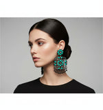 A pair of black earrings with green coloured stone embellishments, displayed on an earring stand.