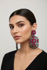 A pair of black earrings with hot pink stone coloured stone embellishments, displayed on an earring stand.