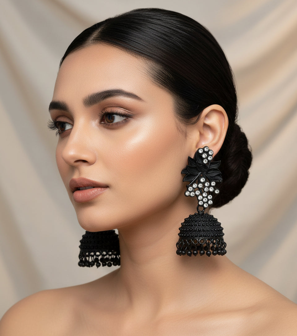 A pair of black jhumki earrings with leaf patterns and silver coloured stones, featuring gold-plated brass metal and nano hangings.
