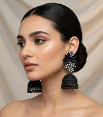 A pair of black jhumki earrings with leaf patterns and silver coloured stones, featuring gold-plated brass metal and nano hangings.