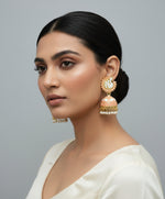 A pair of gold-plated Meenakari peacock Jhumka earrings with Peach and white enamel detailing, displayed on a black stand.