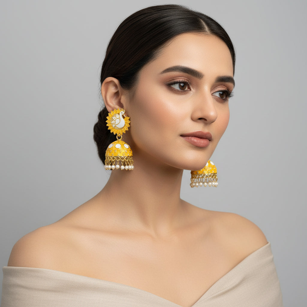 A pair of gold-plated Meenakari peacock Jhumka earrings with yellow and white enamel detailing, displayed on a black stand.