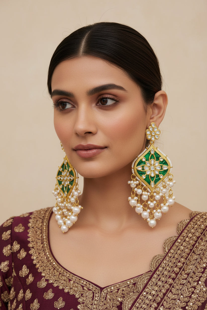 A pair of gold-plated Parul Pearl kundun earrings with intricate designs and drop-shaped pearls, displayed on a stand.