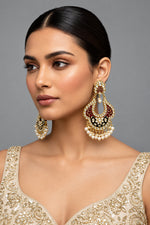 A pair of gold-toned chandbali earrings with maroon and black meenakari and kundan studded details along with pearls.