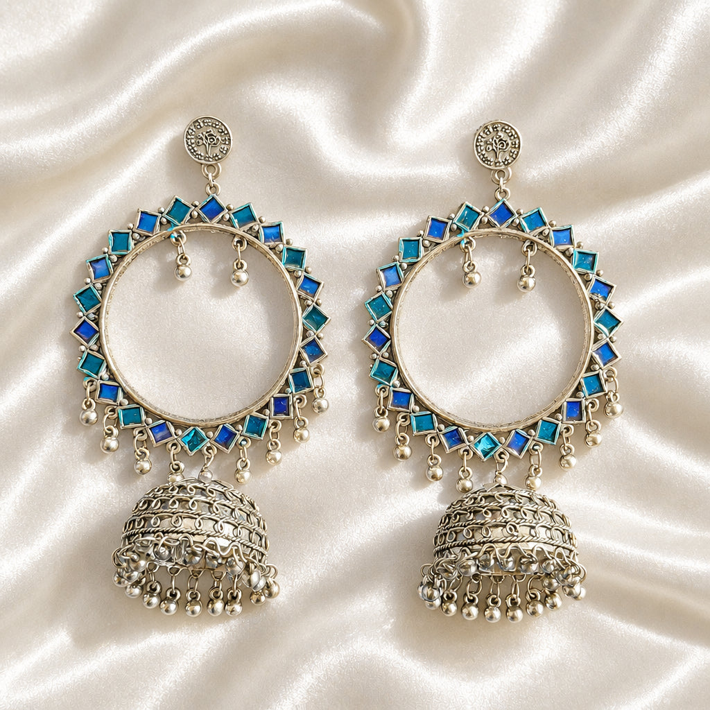 Pair of blue and teal enamel-painted silver-tone hoop jhumka earrings on blue fabric.