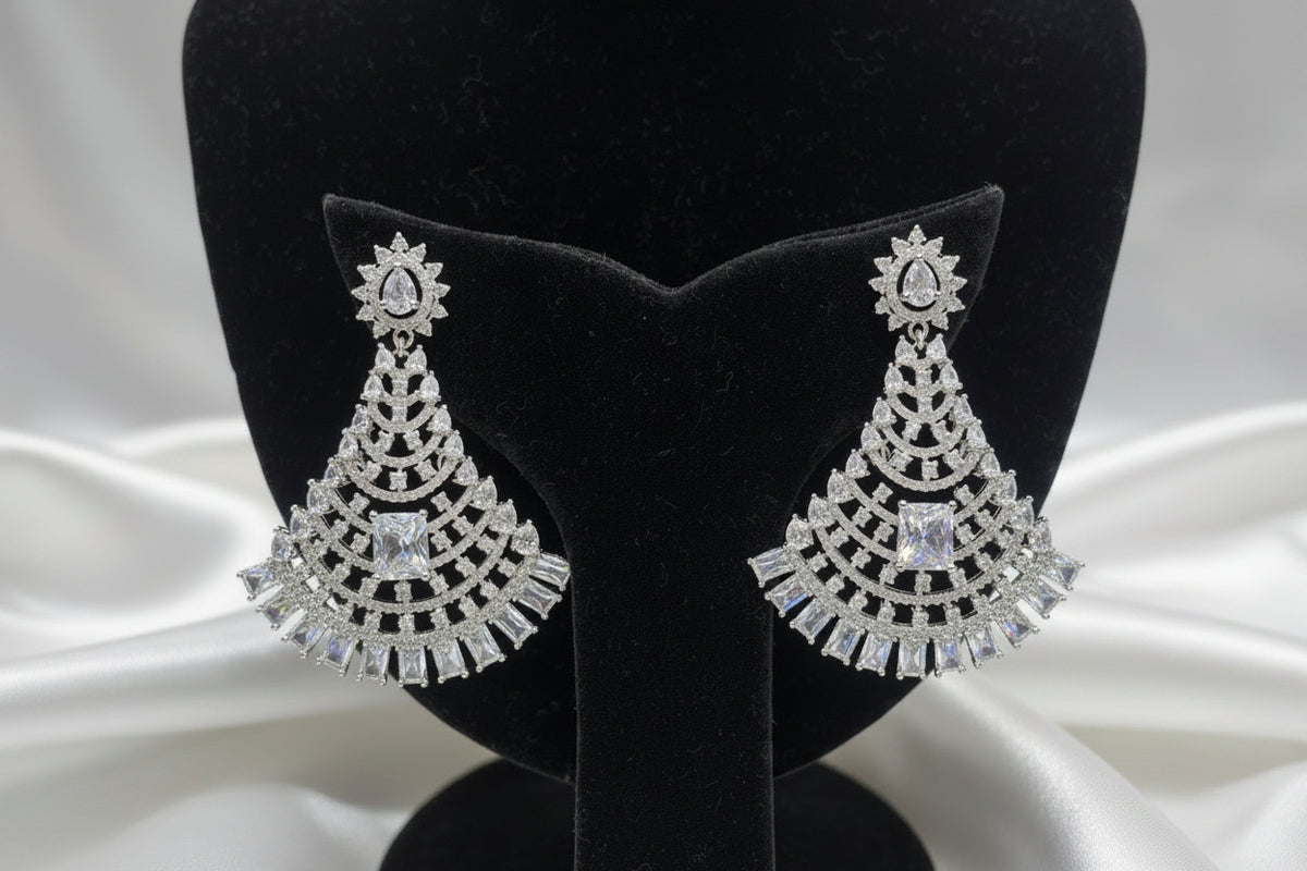 A pair of silver-toned, tiered chandelier-style earrings with clear stones and a central blue stone, displayed on a black velvet jewellery bust inside a shop.