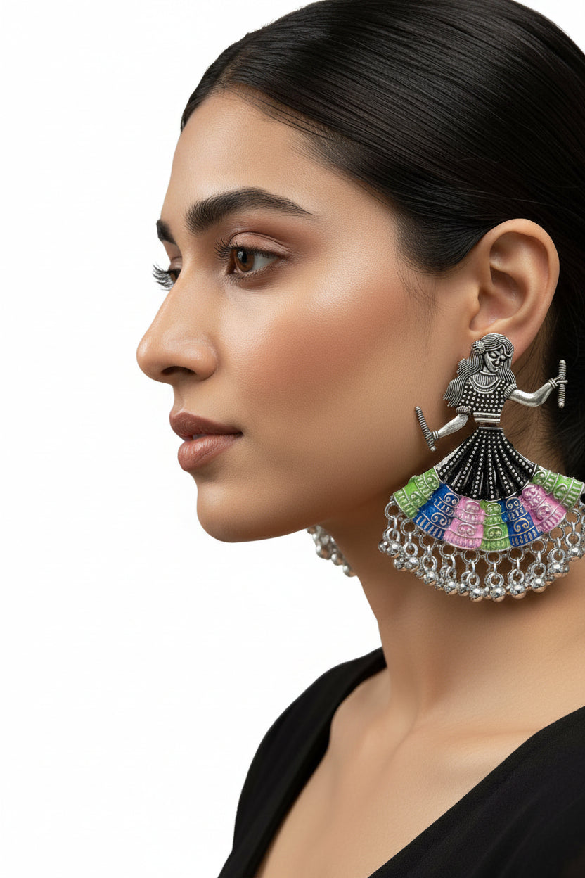 A pair of silver toned metal oxidised earrings design is showing a woman is playing dandiya in navratri lehnga choli traditional dress for navratri nights.
