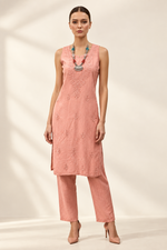A woman modeling a sleeveless peach-pink embroidered kurta with matching wide-leg trousers, styled with a turquoise beaded necklace and nude heels against a plain white background.
