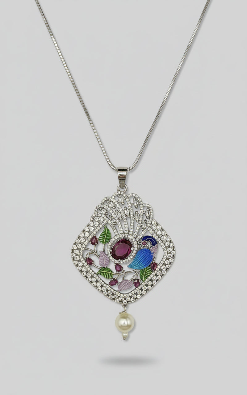 A peacock-shaped necklace pendantwith blue, green, and gold enamel accents and white faux pearl. Pendant in a silver chain is focused in this image.