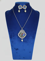 A peacock-shaped pendant necklace with blue, green, and gold enamel accents and white faux pearls, accompanied by matching earrings, displayed on a black mannequin bust.