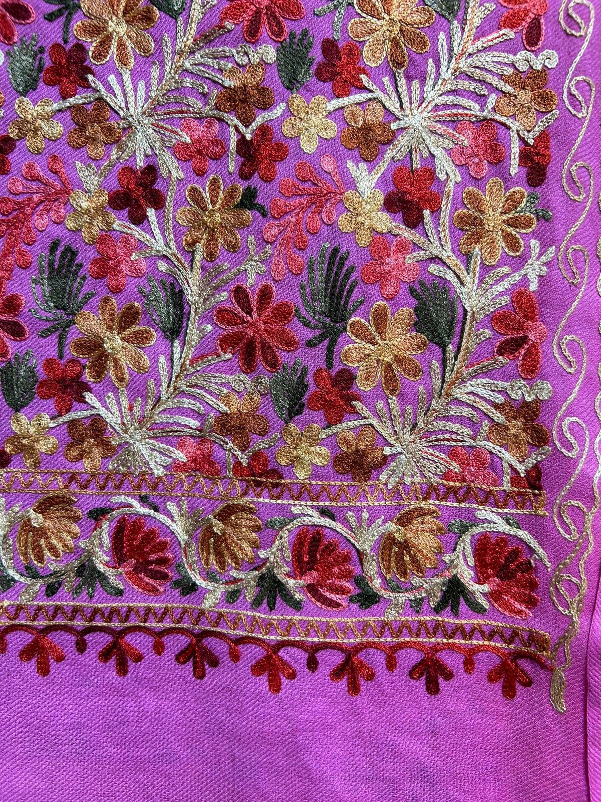 A pink base colour floral multi-colour embroidered shawl in an elegant room with curtains and furniture.