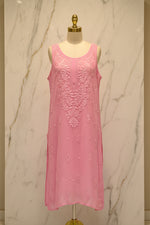 A pink sleeveless tunic dress with intricate floral embroidery and lace detailing, hanging on a white hanger in a retail setting.