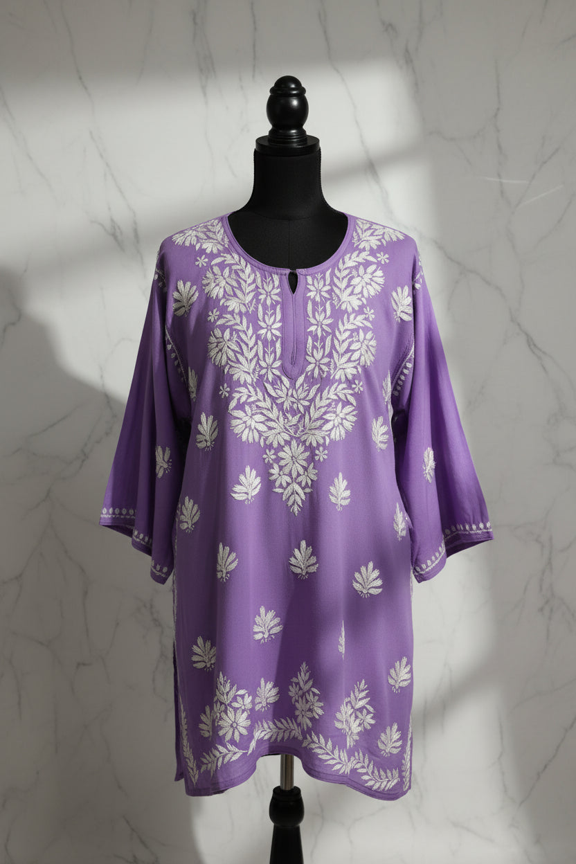 A purple cotton kaftan tunic with white floral and leaf embroidery, hanging on a white hanger against a white background.