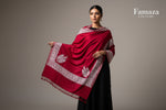 A red colour Kashmiri embroidered pashmina shawl with tassels on the ends, displayed on a wooden surface.