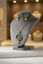 A rhodium-gold plated brass pendant with a peacock design accompanied by earrings, featuring vibrant green, blue, and gold enamel accents, as well as sparkling white and Turquoise AD stones embellishments.