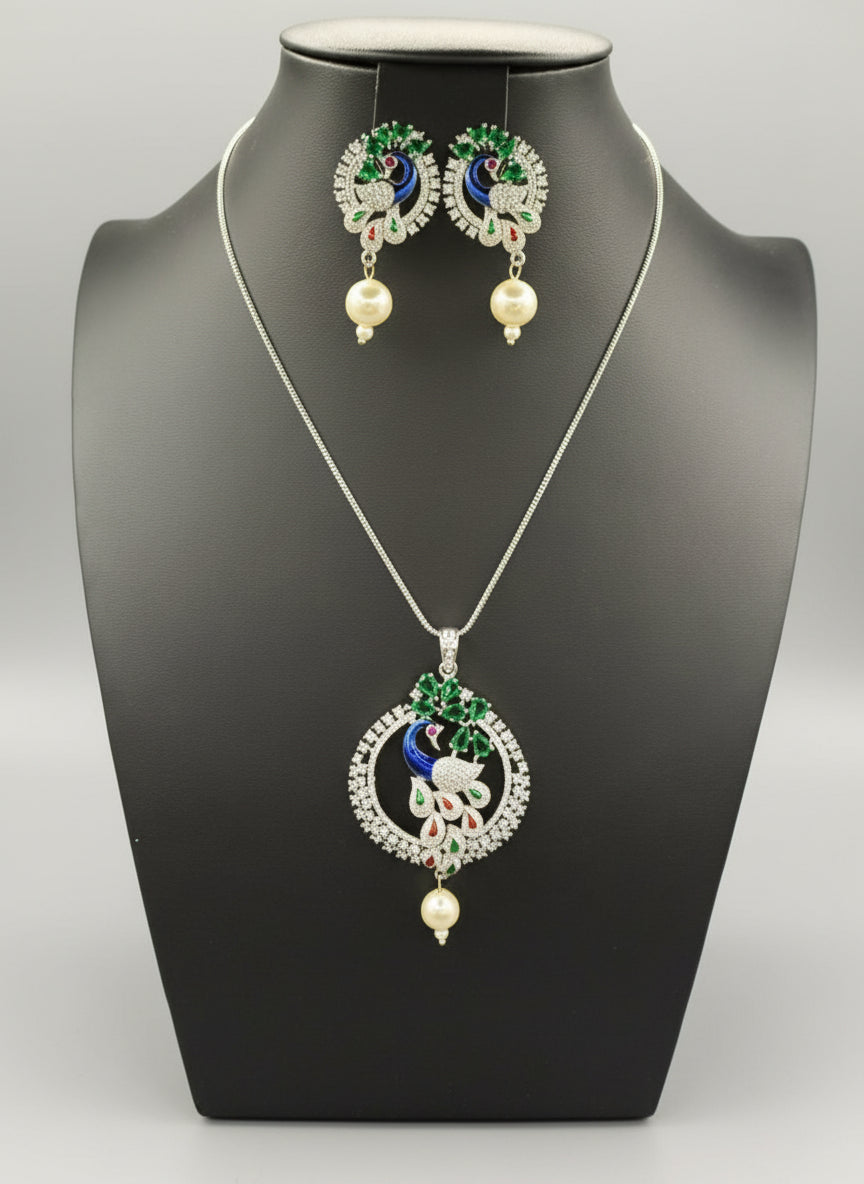 A rhodium-silver plated brass pendant with a peacock design accompanied by earrings, featuring vibrant green, blue, and gold enamel accents, as well as sparkling white and bottle green ad crystal embellishments.
