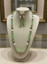 A set of jewellery featuring a long necklace with lime green-coloured glass beads and metallic accents, paired with matching earrings, displayed on a mannequin bust.