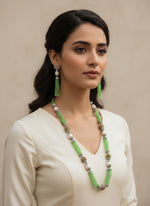 A set of jewellery featuring a long necklace with lime green-coloured glass beads and metallic accents, paired with matching earrings, displayed on a mannequin bust. Party wear set.