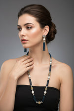 A set of jewellery featuring a long necklace with navy blue glass beads and metallic accents, paired with matching earrings, displayed on a mannequin bust.