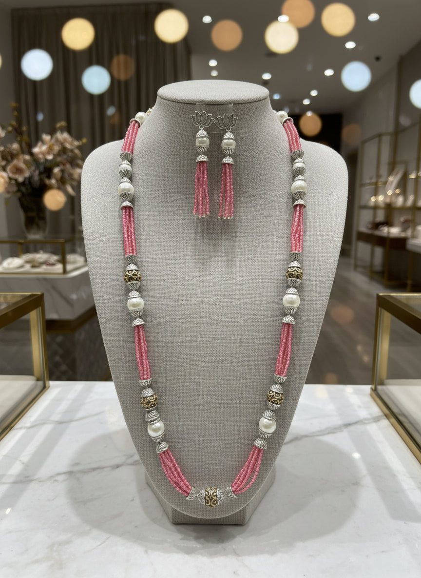 A set of jewellery featuring a long necklace with pink-coloured glass beads and metallic accents, paired with matching earrings, displayed on a mannequin bust. Party wear set.