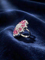 A silver-tone floral cluster ring featuring large oval pink gemstones and smaller clear stones, displayed on a dark navy blue velvet fabric background.