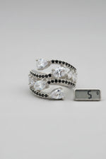 A silver-toned wrap cuff ring with marquise and oval iridescent clear stones and small dark accent stones, displayed on a black textured surface.