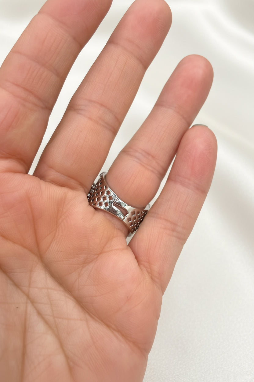 A silver textured band ring worn on a person's ring finger, shown in a close-up shot of the hand against a black background.