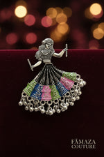 A silver tone meta oxidised earring design is showing a woman is playing dandiya in navratri lehnga choli traditional dress for navratri.