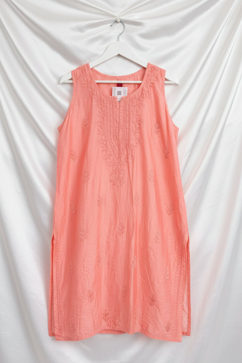 A sleeveless coral pink embroidered top with matching trousers laid out on a black surface, held up by a hand. The top features tonal floral embroidery around the neckline and scattered motifs across the fabric.