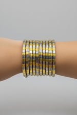 A stack of multiple bangle bracelets with alternating yellow-gold and silver metallic segments, worn on a person's wrist against a dark background.