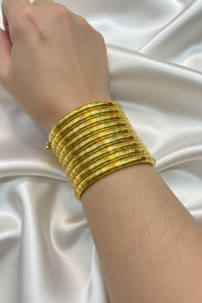 A stack of ten textured gold bangles worn on a person's wrist, shown against a black background.