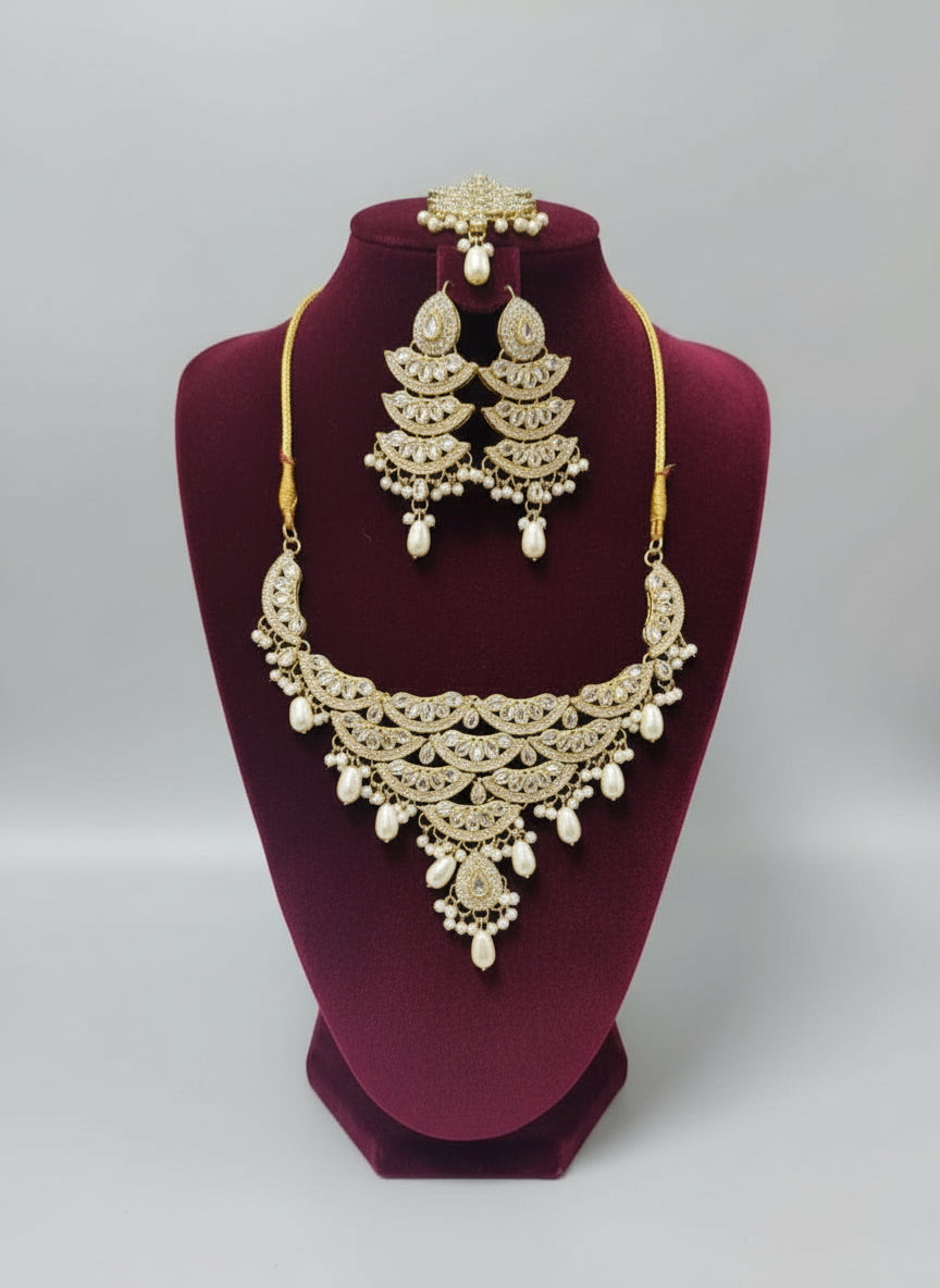 A traditional bridal necklace set featuring drop pearls and oval Kundans, with matching earrings and a maang tikka, displayed on a mannequin.